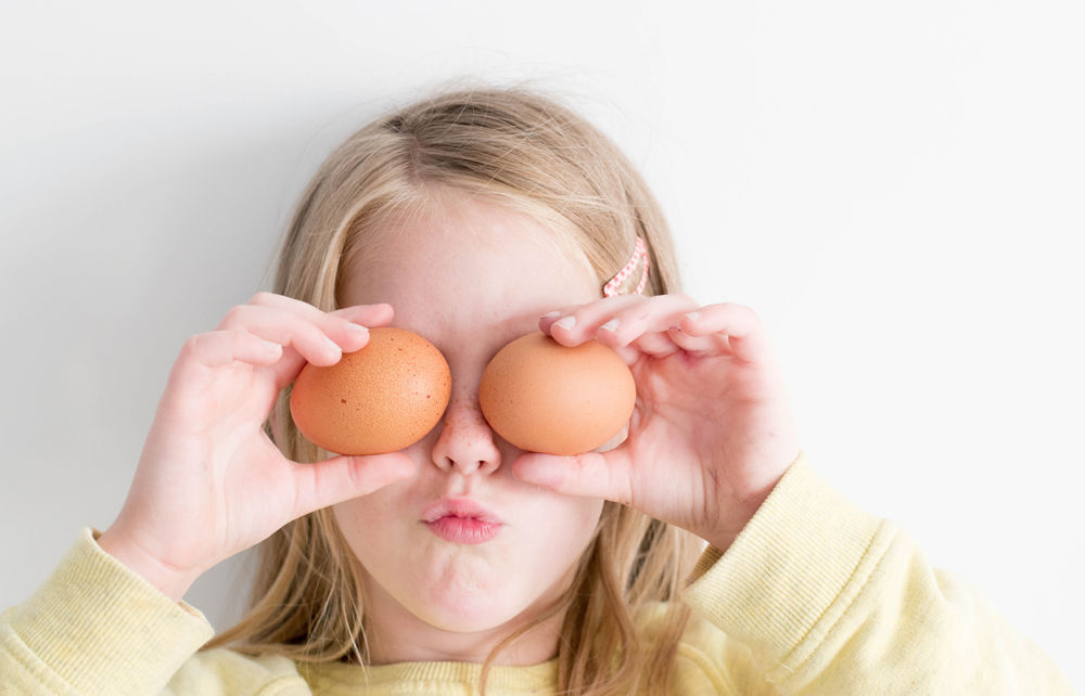 Familen-Spiel-Oase-Frühstück Ein Mädchen hält sich Frühstückseier vor ihre Augen